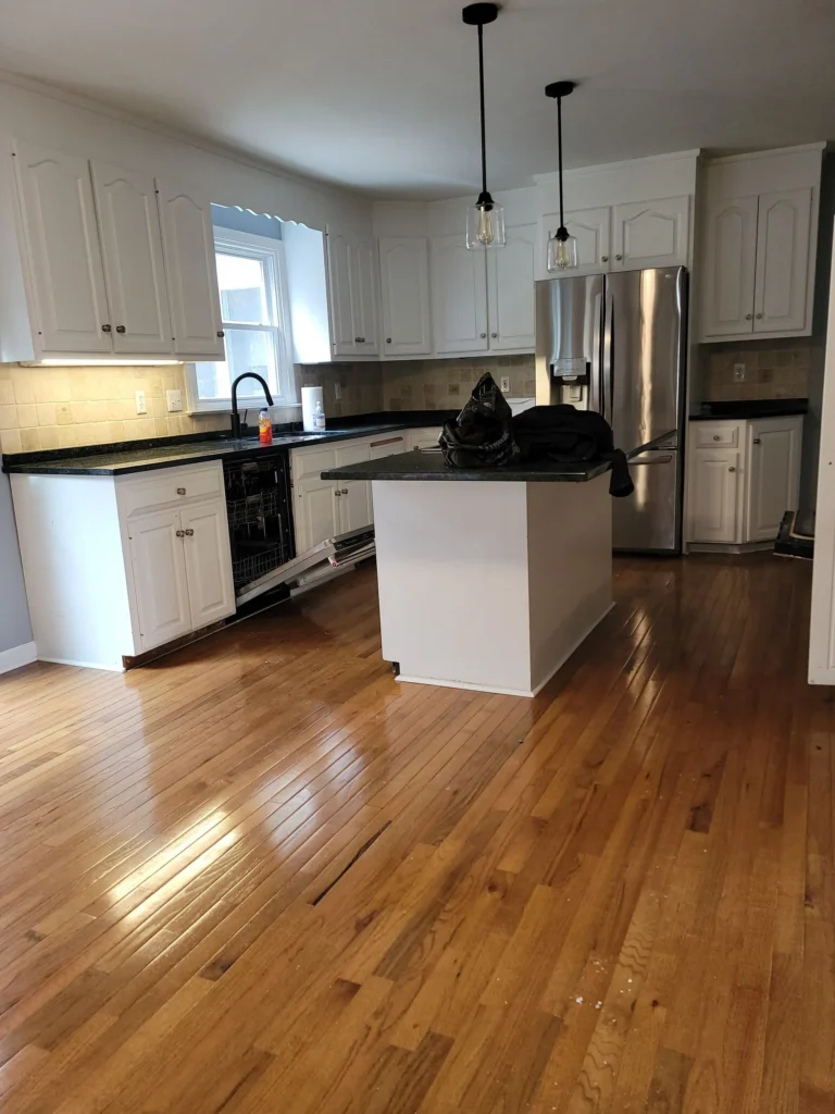Clean kitchen with white cabinets, black countertops, and polished hardwood flooring