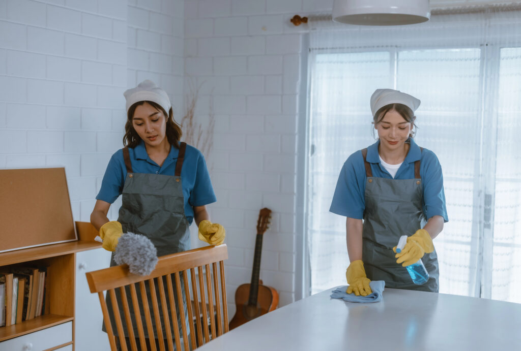 Professional cleaners wiping down a dining table and dusting a wooden chair in a bright, modern home in Connecticut