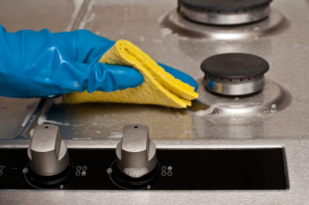 Cleaning a stainless steel stove with a sponge and gloves during appliance deep cleaning service