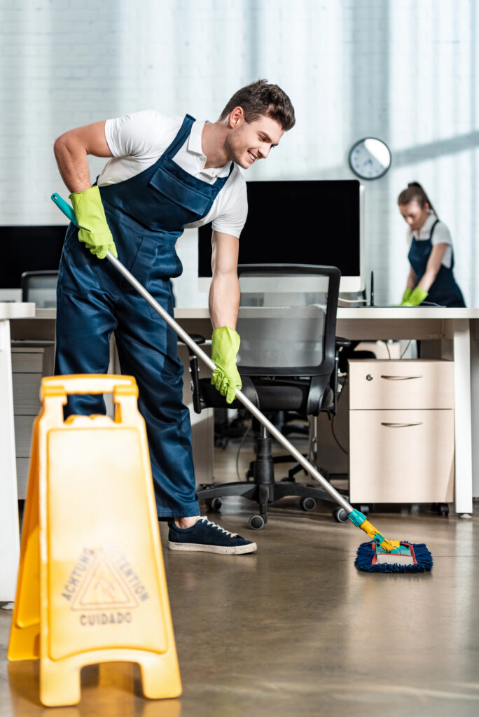 Janitor mopping a modern office floor in Connecticut with caution sign in foreground.
