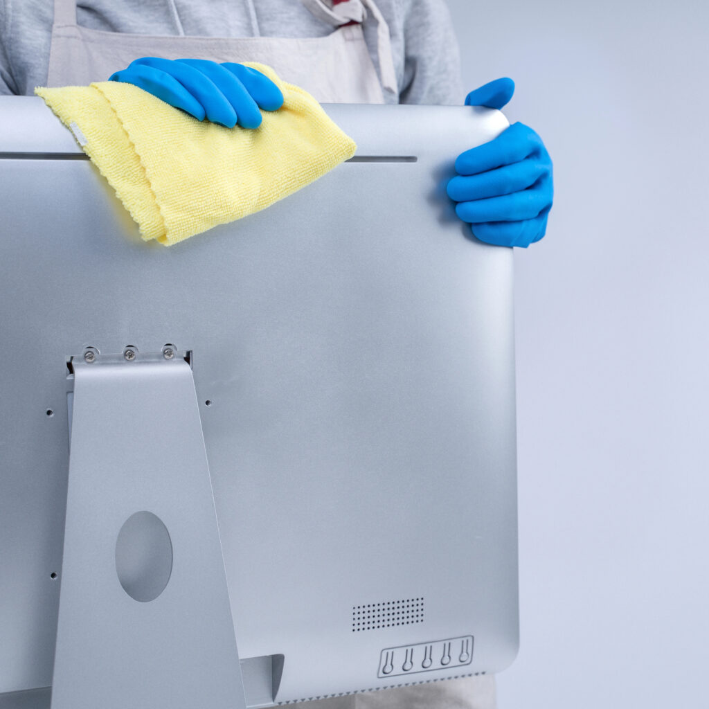 Person in blue gloves wiping a computer monitor with a yellow microfiber cloth in a Connecticut office.