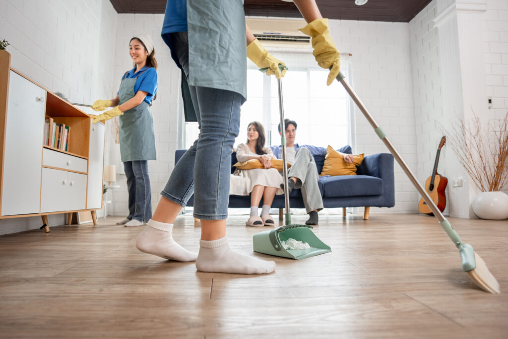 Cleaning team performing deep cleaning in a bright living room while homeowners relax on the couch