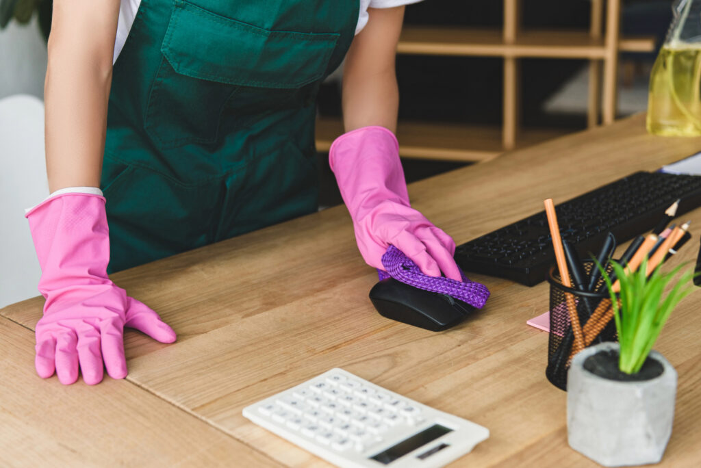 Woman cleaning a home office desk with gloves and cloth