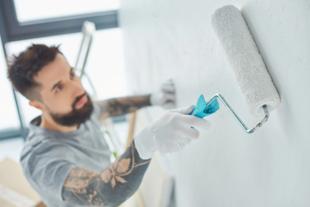 Bearded man painting an interior wall with a roller brush in a well-lit Connecticut home