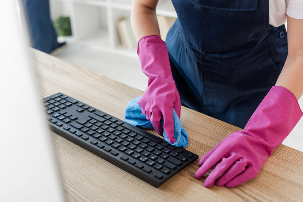 Close-up of a cleaner wearing pink gloves sanitizing an office keyboard with a microfiber cloth in Connecticut.