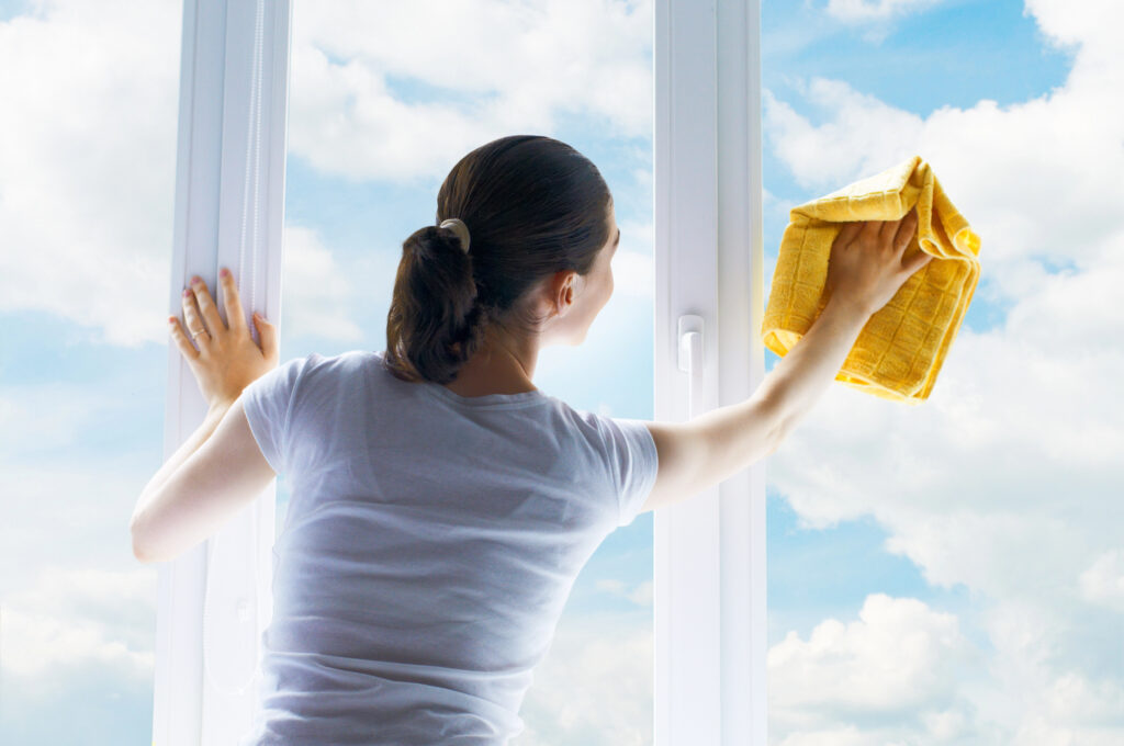 Woman cleaning interior home window with yellow cloth for streak-free finish